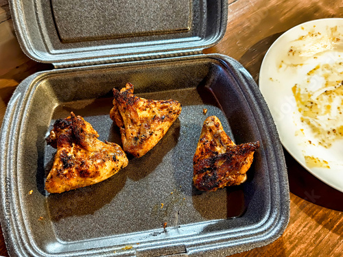 Grilled chicken wings served in a takeout container on a wooden table during dinner time