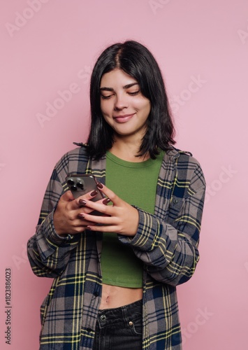Young woman smiling while texting on her phone in front of a pink background