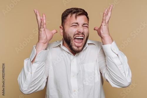 Man expresses frustration with hands raised while yelling against a plain background