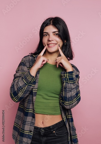 Smiling young woman making a playful gesture against a pink background in a casual setting with natural light