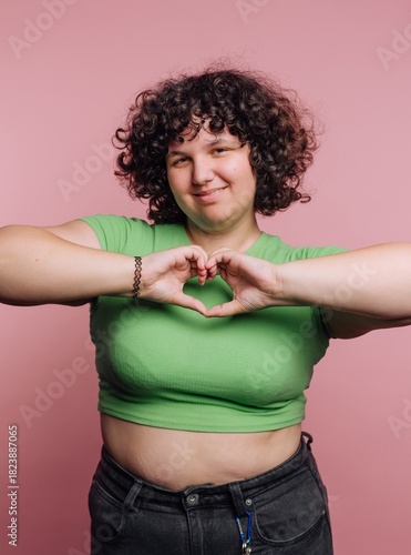 Fotografie Curly-haired person showing love with heart-shaped hands against a pink backgrou