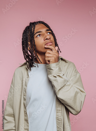 Young man with braided hair thinks thoughtfully against a pink background in a creative studio setting