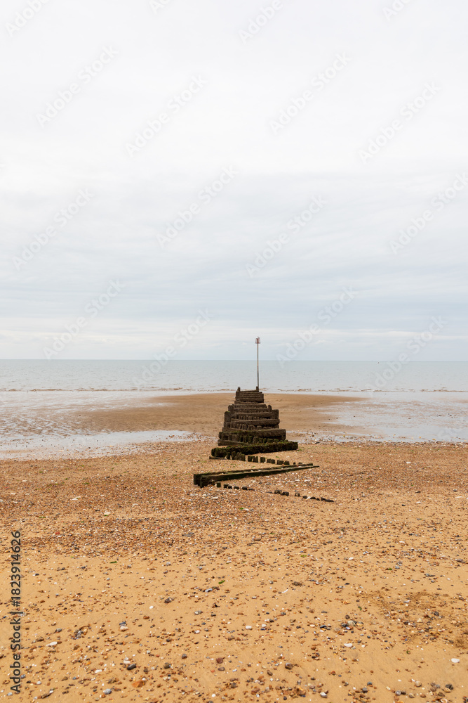 Fototapeta premium Minimalist beach breakwater waves stopper extending into calm sea under soft cloudy sky