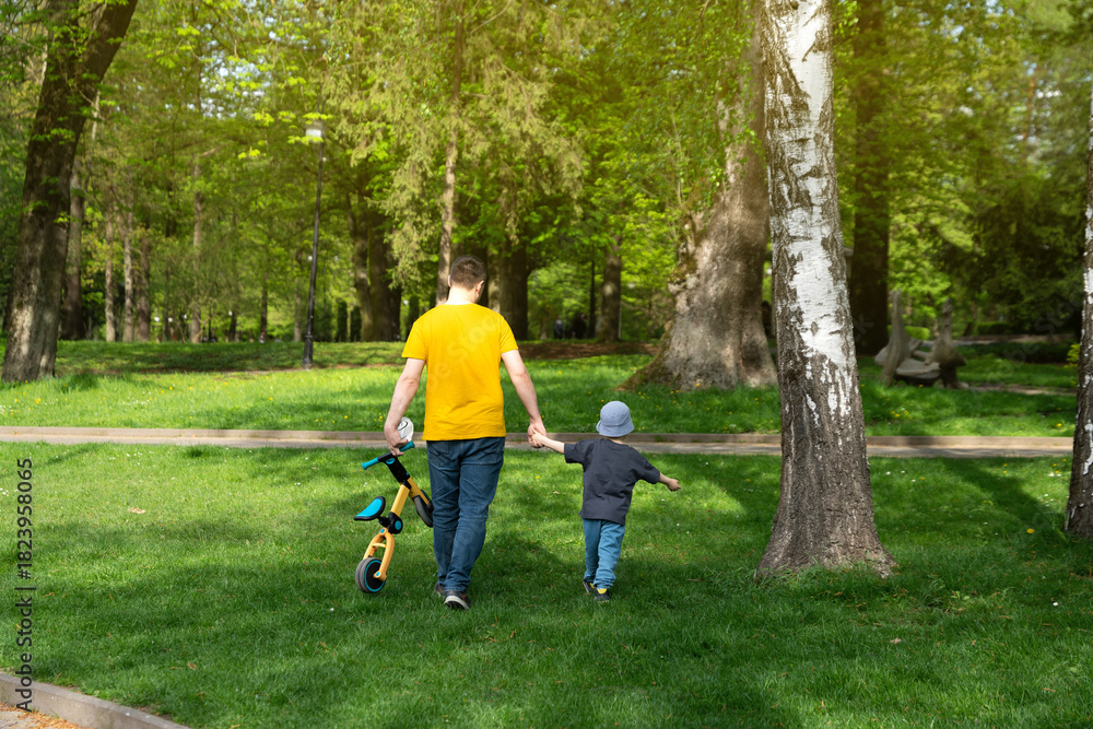 Fototapeta premium Father and son walking in the park holding hands on a sunny spring day. Family time and leisure. Lifestyle