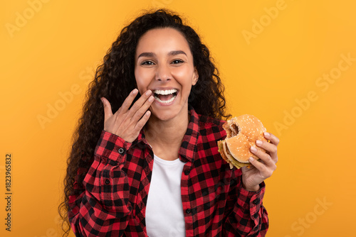 Fotografie A joyful woman laughs while holding a tasty burger, enjoying her cheat meal