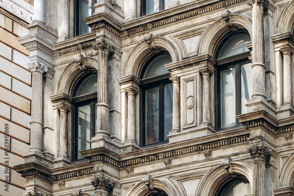 Fototapeta premium A detailed view of a historic stone facade in downtown Montreal, featuring arched windows, classical columns, ornate carvings, and rich architectural textures.