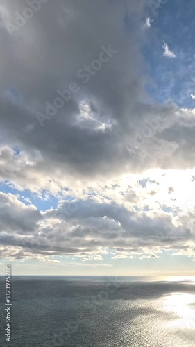Ocean, Sky, Clouds vast expanse under dynamic partly cloudy blue sky, sunlight reflecting on shimmering water surface. Vertical video.