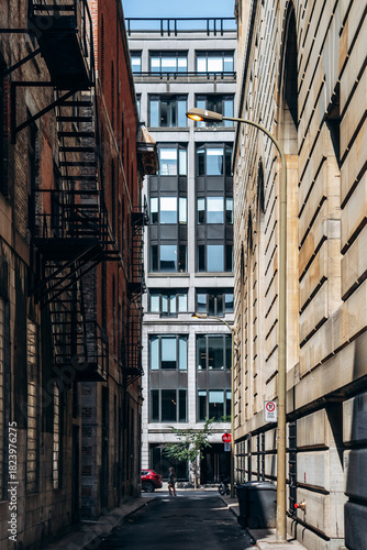 Montreal, Canada - August 14, 2025: narrow alleyway between historic and modern buildings with fire escapes and person walking