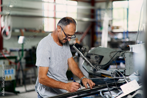 Factory worker examining metal material in industrial workshop, representing quality control, inspection, and manufacturing process.