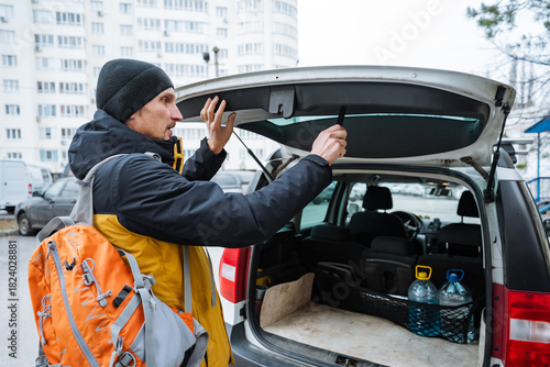 preparing vehicle for outdoor adventure, individual organizing backpacks and water bottles for outdoor trip, person arranging camping equipment and hydration supplies in vehicle before hike