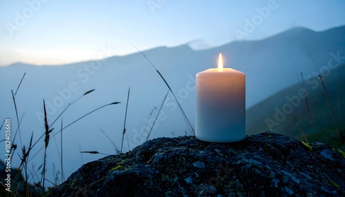 Vela encendida sobre roca en paisaje montañoso al amanecer con niebla suave y atmósfera tranquila