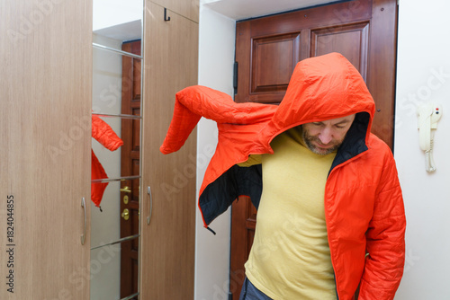 Man putting on a bright orange hooded jacket in a hallway. Getting ready to leave the house