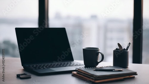Modern Office Desk Setup With Laptop Mug Notebook And Pens Against Blurred Cityscape Background At Dusk
