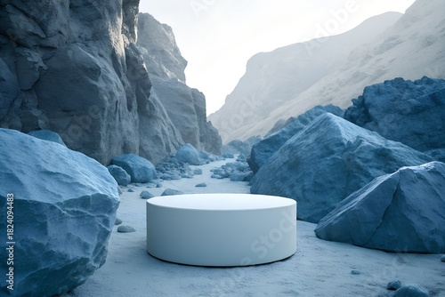 A white cylindrical pedestal stands centered in a rocky, blue-toned canyon under soft, diffused light, creating a serene, minimalist, and otherworldly atmosphere.
