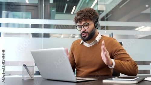 Confident businessman in a headset talking on a video call using laptop computer sitting in office. A male manager has a remote business meeting. male professional communicates at an online conference