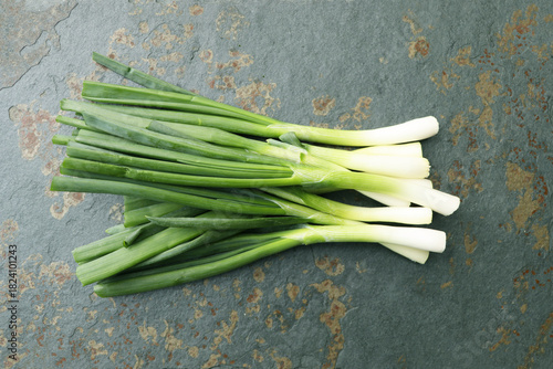 Young and fresh bunch of green onions or scallions placed on stone background.