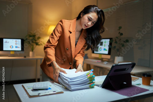 Asian businesswoman managing paperwork late working in office