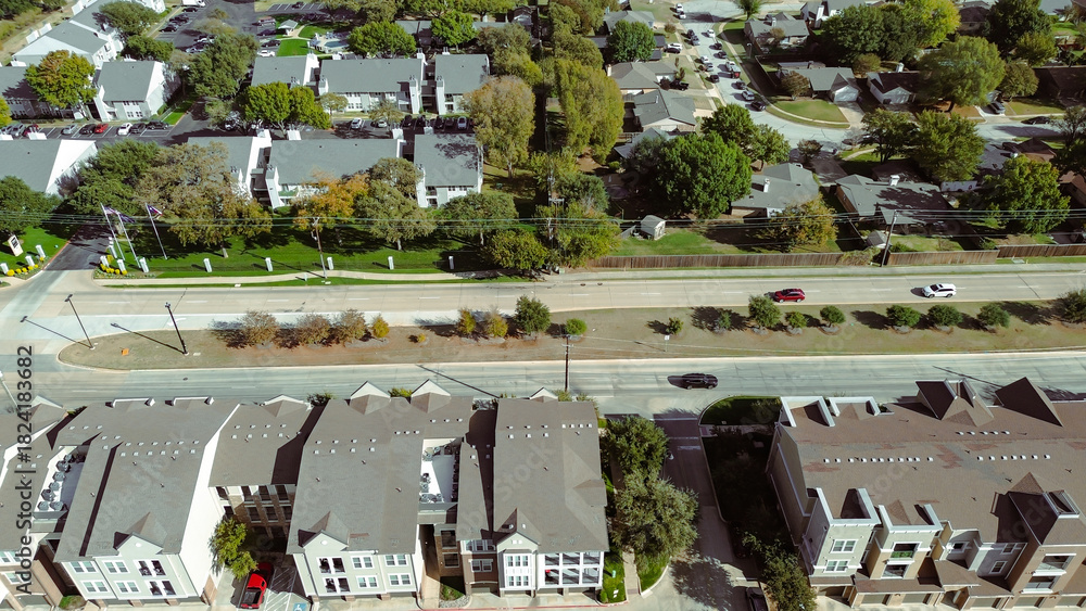 Obraz premium Modern townhouses with uniform architecture and driveways, separated by main road from single-family homes. Background reveals dense suburban sprawl and tree-lined streets in Flower Mound, Texas