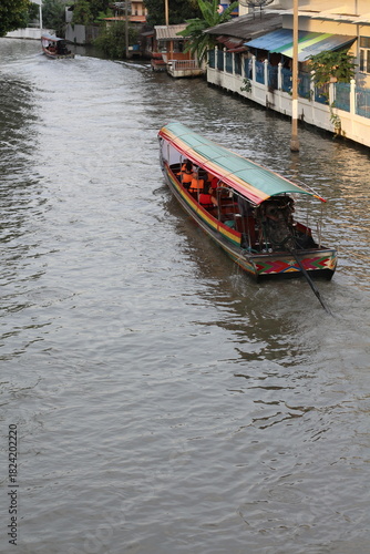 Photography Longtail boat navigating a canal in Bangkok, Thailand, on a sunny day