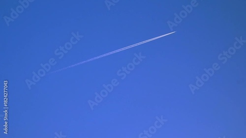 Jetliner flies through clear blue sky, leaving behind beautiful white contrail. Plane glides smoothly across the sky. Not AI