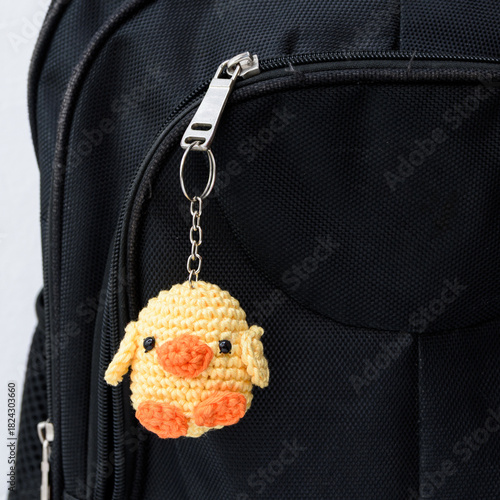 Plush duck keychain made using the amigurumi technique in yellow and orange, hanging on a school backpack.