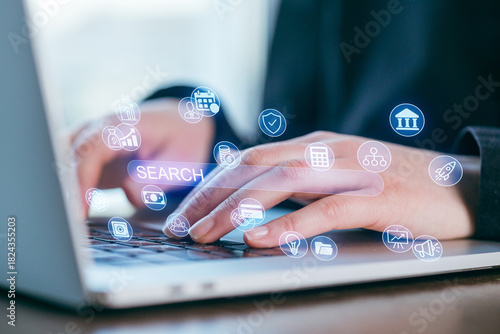 Hands typing on a laptop keyboard with search icons above in a bright workspace