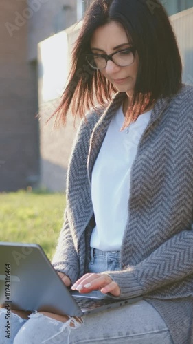 Young caucasian woman university student learning online using laptop computer, taking notes, studying outdoor sitting outside uni campus area at sunny weather. Slow motion