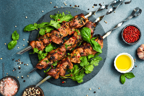 Foto Delicious juicy skewers with pork meat grilling, grilled pork kebabs on a stone slate plate