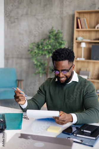 Black man smiling working documents at office desk