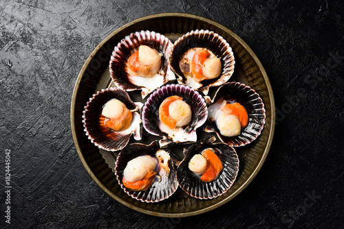 Seafood. Metal tray with Fresh Sea Scallops in shells. On a dark stone background. Top view.