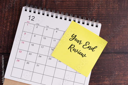 December calendar with a yellow note reading ‘Year End Review’ on wooden desk.