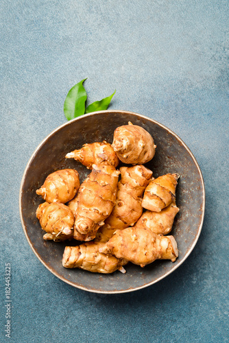Organic raw Jerusalem artichoke root in a ceramic bowl. On a gray stone background. Close-up. Free space for text. © Yaruniv-Studio