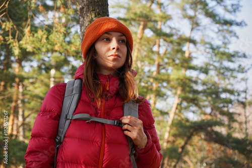 A young tourist in bright clothes with a backpack is standing in the forest, admiring the scenery. Hiking in the autumn forest alone, solo camping.