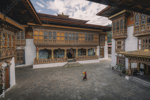 Punakha, Bhutan - 19 September 2025: View of a solitary monk walking across the stone courtyard, framed by the intricate woodwork and vibrant colors of Punakha Dzong's architecture.