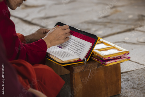 View of a monk, bathed in warm hues, engrossed in ancient scripts within a vivid yellow case, seated serenely on a wooden stool, Wolakha Nunnery, Punakha, Bhutan.