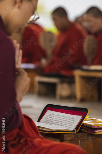 View of monks in vibrant red robes chanting from sacred texts, their devotion palpable in the tranquil air, Wolakha Nunnery, Punakha, Bhutan.