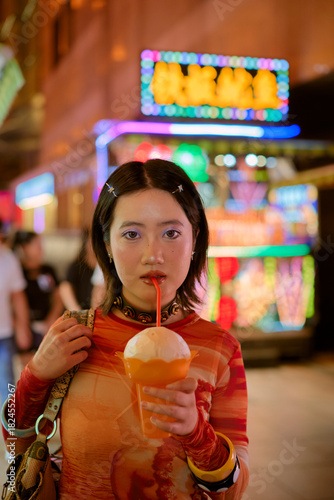 Young woman in a vibrant outfit drinks from a cup with a colorful city backdrop. Shanghai, China
