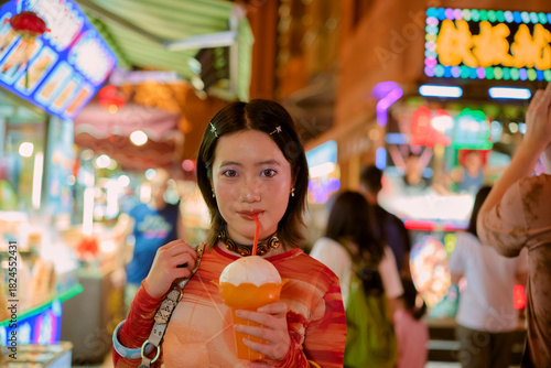 Young woman in vibrant market drinking bubble tea under colorful neon lights at night. Shanghai, China