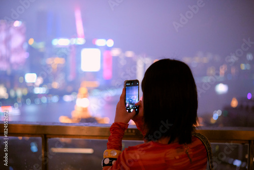 Woman in vibrant shirt taking a cityscape photo with a phone from a high vantage point. Shanghai, China