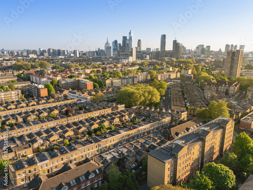 Aerial view of a cityscape with dense housing and skyscrapers under a clear blue sky. London, UK