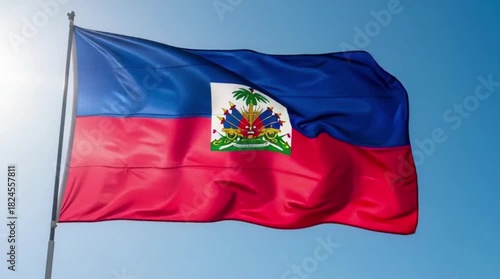 The national flag of Haiti with its coat of arms, waving proudly in the wind against a bright blue sky.