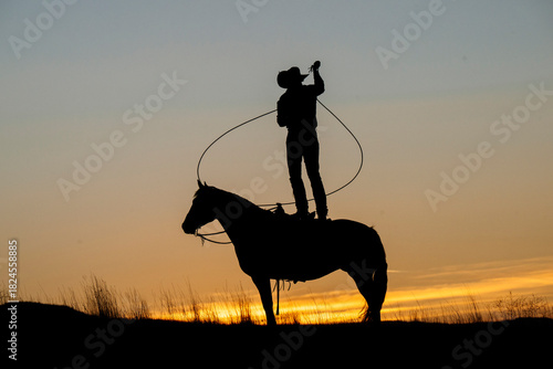 Silhouette of a cowboy on horseback lassoing at sunset with a vibrant sky. Oregon, USA