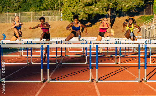 Five female athletes in colorful sportswear compete in a hurdle race on a sunny track. WA, USA