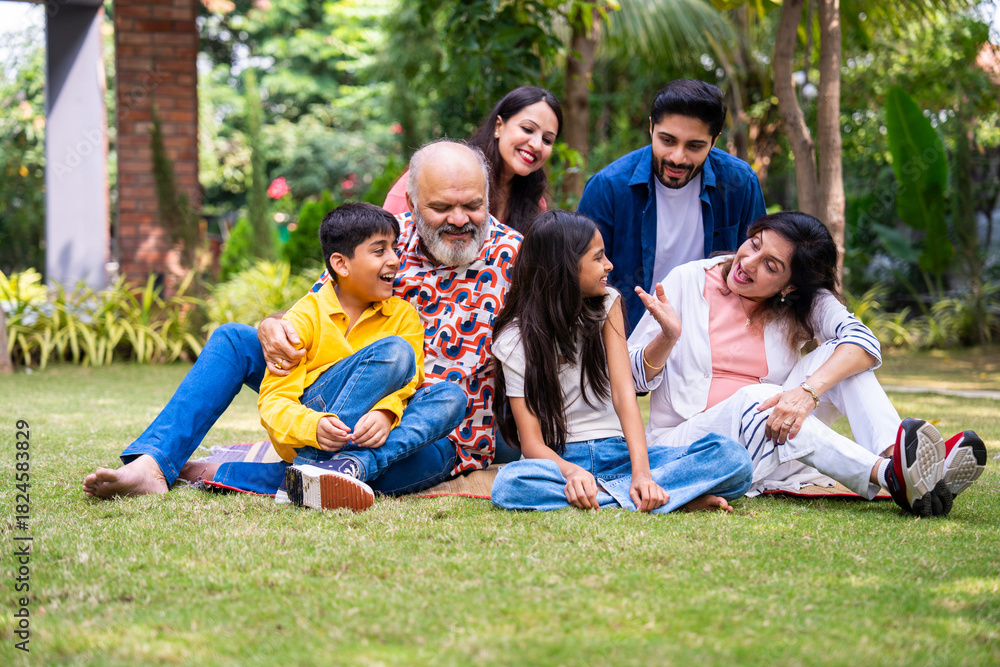 Fototapeta premium Indian family of three generations smiling and bonding outdoors on green park lawns