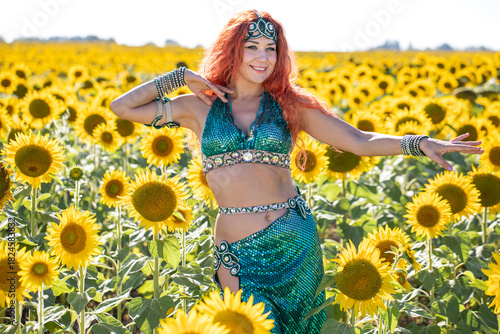 A red-haired oriental dancer poses in a field of sunflowers.