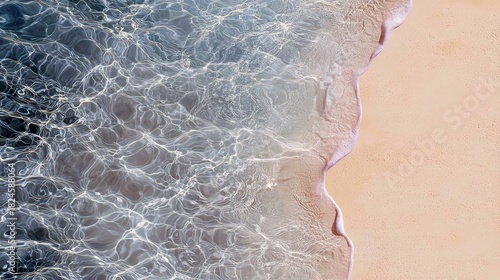 Fototapeta Naklejka Na Ścianę i Meble -  A serene aerial view shows the edge of a sandy beach meeting clear ocean water. Sunlight creates shimmering patterns on the water's surface as a gentle wave was
