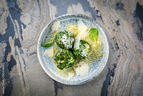 Artisan homemade Austrian spinatknödel - bread knodel dumpings with melted butter and parmesan served as top view on a design plate