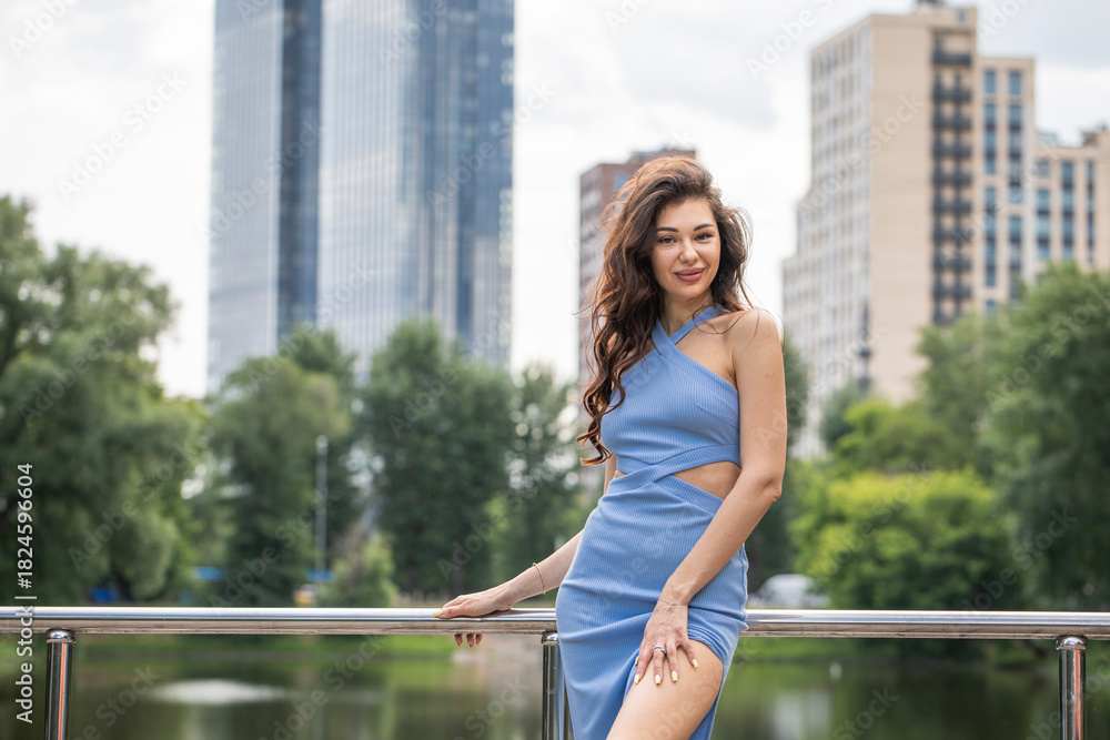 Fototapeta premium Young beautiful brunette woman in blue knitted dress posing in summer park