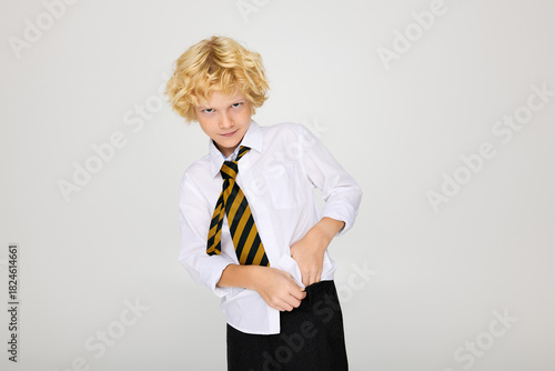 Blonde boy in wavy hair adjusts his striped tie while posing in studio