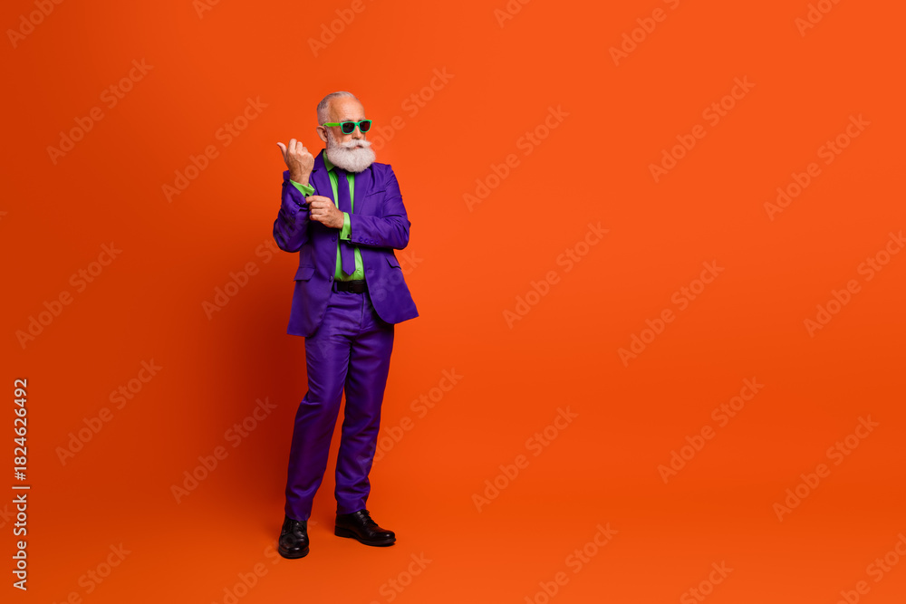Fototapeta premium Modern retro styled elderly man in purple suit and green tie posing against bright orange background